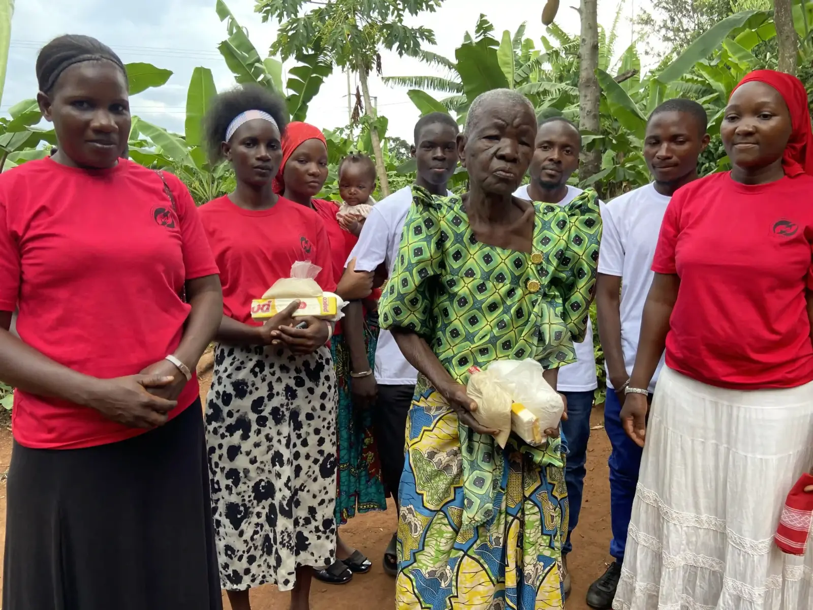 Volunteers in red shirts standing with an elderly woman holding a bag of supplies