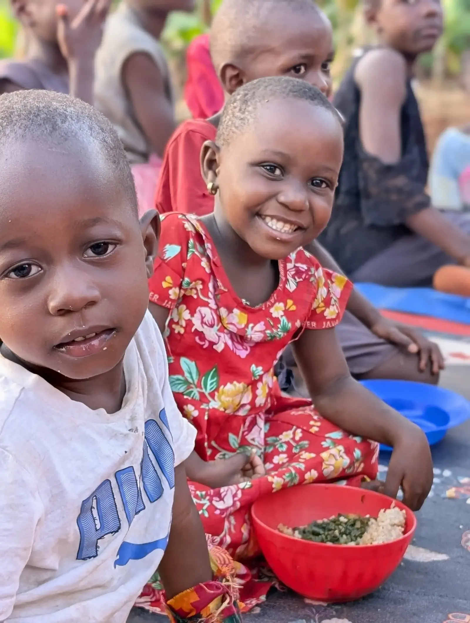 A smiling girl in a red dress sitting with other children at a meal