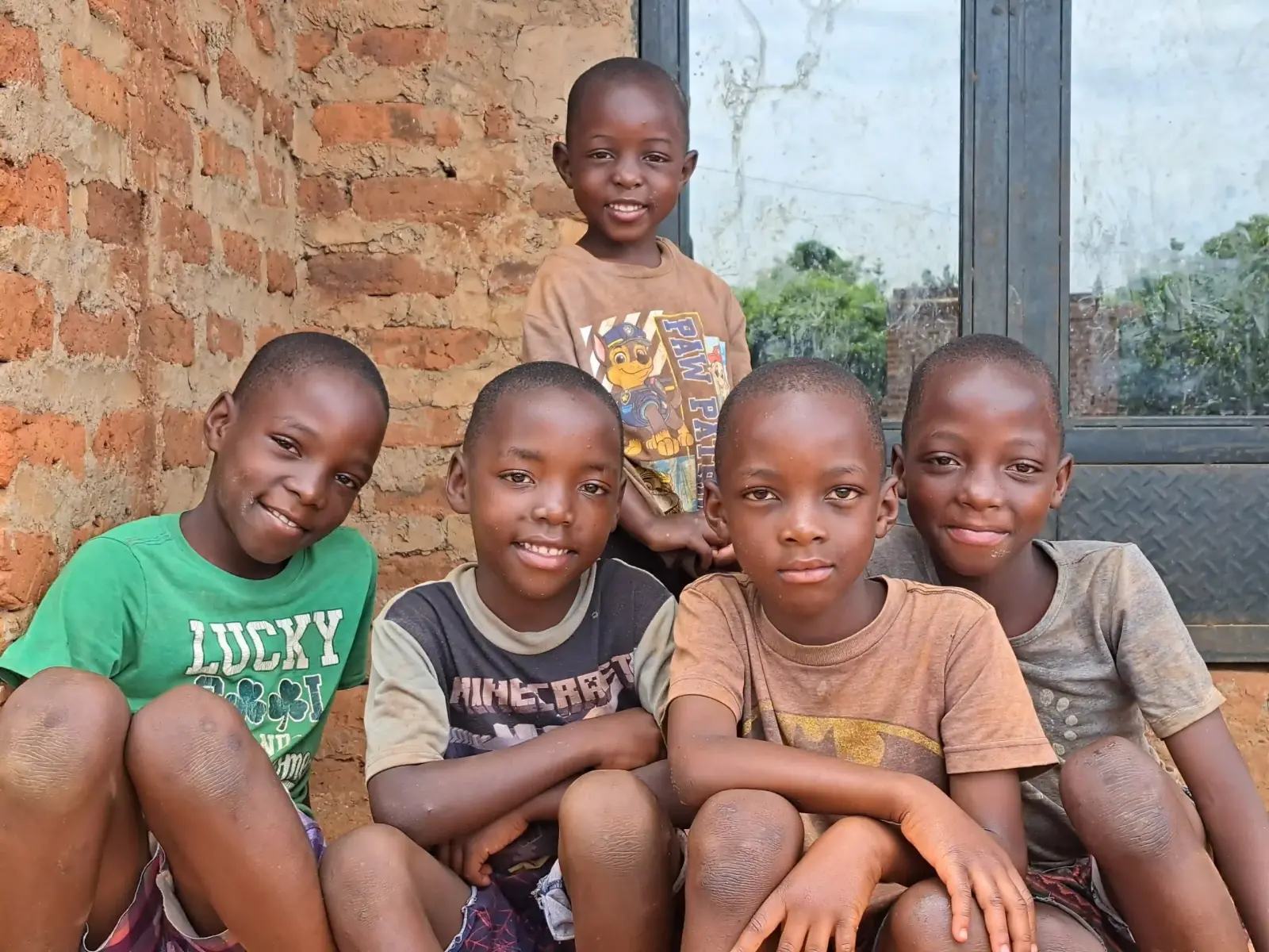 Five boys sitting close together and smiling against a brick wall